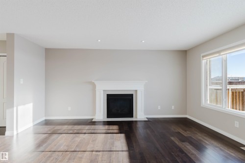 Spacious room featuring dark wood-finish flooring, a white mantel fireplace, large windows with white trim, recessed lighting, and light neutral wall colors - 16627 18 Avenue, Edmonton, AB - Indoor Photo Showing Living Room With Fireplace