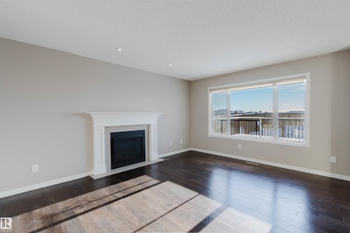Spacious living area featuring a decorative fireplace with white mantel, dark wood-finish flooring, recessed lighting, and a large multi-pane window - 16627 18 Avenue, Edmonton, AB - Indoor Photo Showing Living Room With Fireplace