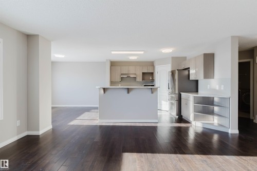 Open-concept kitchen and living area featuring dark wood-finish flooring, light-toned cabinetry, light countertops, and stainless steel appliances - 16627 18 Avenue, Edmonton, AB - Indoor Photo Showing Kitchen