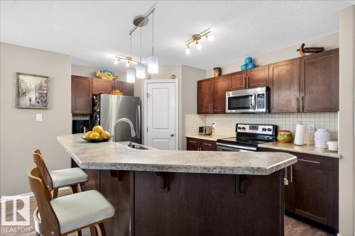 Kitchen featuring an island with a breakfast bar, dark wood-finish cabinetry, stainless steel appliances, and a tiled backsplash - 18080 89 Street, Edmonton, AB - Indoor Photo Showing Kitchen With Upgraded Kitchen