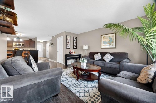 Open-concept living area featuring wood-finish flooring, neutral wall tones, recessed lighting, and a partial view of the kitchen with dark cabinetry and stainless steel appliances - 18080 89 Street, Edmonton, AB - Indoor Photo Showing Living Room