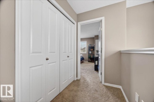 Hallway featuring two white bi-fold closet doors, neutral tone wall paint, textured carpet flooring, and white trim - 18080 89 Street, Edmonton, AB - Indoor Photo Showing Other Room