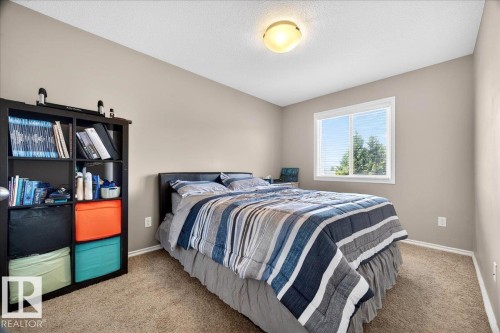 Carpeted bedroom featuring a large window with white blinds, light beige wall paint, a built-in shelf unit, and a flush-mount ceiling light fixture - 18080 89 Street, Edmonton, AB - Indoor Photo Showing Bedroom