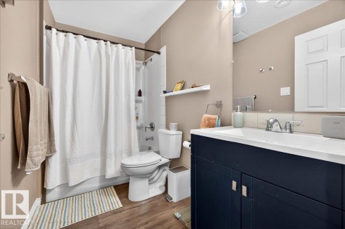 Bathroom featuring a dark blue vanity with a white countertop and integrated sink, a full-width mirror, and wood-finish flooring - 18080 89 Street, Edmonton, AB - Indoor Photo Showing Bathroom
