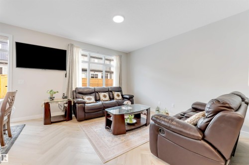 Living area featuring light wood-finish flooring with a herringbone pattern, recessed ceiling lighting, and large windows with white trim - 6404 27 Avenue, Edmonton, AB - Indoor Photo Showing Living Room