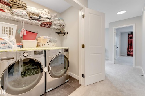 Dedicated laundry area featuring stainless steel front-loading washer and dryer units, dark tile flooring, and overhead wire shelving - 6404 27 Avenue, Edmonton, AB - Indoor Photo Showing Laundry Room