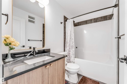 Bathroom featuring a wood-finish vanity with a built-in sink, dark countertop, and matte black faucet - 6404 27 Avenue, Edmonton, AB - Indoor Photo Showing Bathroom
