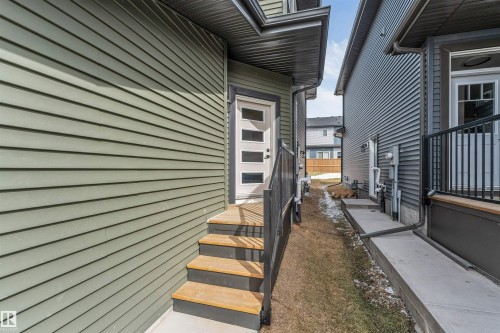 Rear exterior entrance featuring a modern white door with frosted glass panels, wood-finish stairs, and black metal railings - 6404 27 Avenue, Edmonton, AB - Outdoor With Exterior