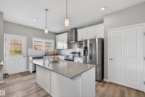 Kitchen featuring a center island with a light-toned countertop, stainless steel appliances, white cabinetry, subway tile backsplash, and wood-finish flooring - 22638 99A Avenue, Edmonton, AB - Indoor Photo Showing Kitchen With Upgraded Kitchen
