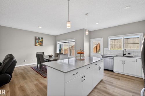 Open-concept kitchen featuring a central island with a light-toned countertop, white cabinetry with dark hardware, stainless steel appliances, and a subway tile backsplash - 22638 99A Avenue, Edmonton, AB - Indoor Photo Showing Other Room
