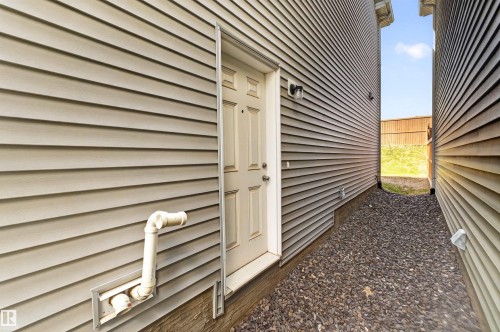 Side exterior entry featuring an outdoor light fixture, light-colored siding, and a gravel walkway - 22638 99A Avenue, Edmonton, AB - Outdoor