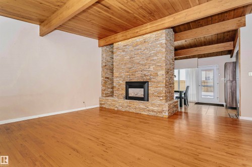 Living area featuring exposed wood beam ceilings, hardwood floors, and a stone-clad fireplace - 24 Sable Crescent, St. Albert, AB - Indoor Photo Showing Living Room With Fireplace