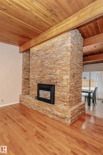 Living area featuring hardwood flooring, a stone fireplace, and a wood-paneled ceiling with exposed beams - 24 Sable Crescent, St. Albert, AB - Indoor Photo Showing Living Room With Fireplace