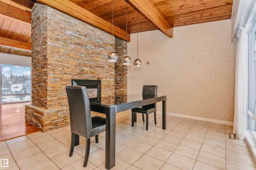 Dining area featuring a stacked stone fireplace, exposed wood beam ceiling, tile flooring, and large windows - 24 Sable Crescent, St. Albert, AB - Indoor Photo Showing Dining Room With Fireplace