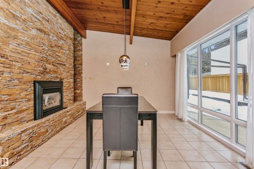 This dining area features a stone-clad fireplace and a wood plank ceiling with exposed beams - 24 Sable Crescent, St. Albert, AB - Indoor With Fireplace
