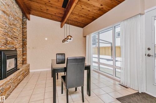 This dining area features a vaulted wood plank ceiling with exposed beams and a stone-clad fireplace - 24 Sable Crescent, St. Albert, AB - Indoor Photo Showing Other Room With Fireplace