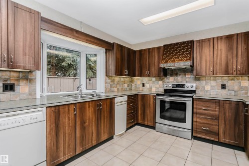 The kitchen features extensive dark wood cabinetry, a bay window over the sink, and a stainless steel oven - 24 Sable Crescent, St. Albert, AB - Indoor Photo Showing Kitchen With Double Sink