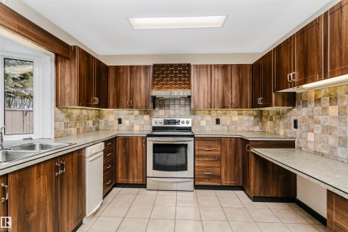 Well-appointed kitchen featuring extensive cabinetry, stainless steel oven with stovetop, tile backsplash, and a double basin sink - 24 Sable Crescent, St. Albert, AB - Indoor Photo Showing Kitchen With Double Sink