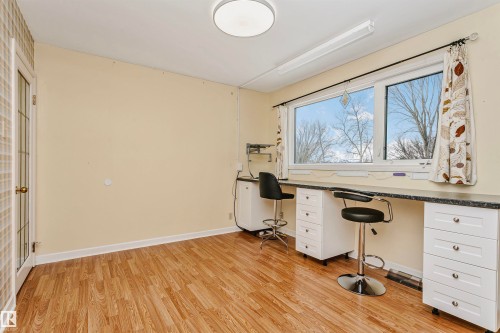 Room featuring wood-look flooring, a window providing a view of outdoor trees, and a built-in desk with white cabinetry - 24 Sable Crescent, St. Albert, AB - Indoor Photo Showing Office