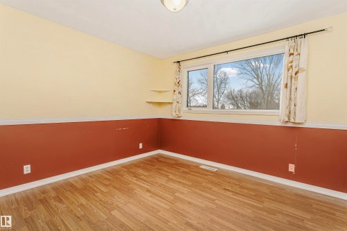 This room features wood-look flooring, a window with a view of trees, and two wall-mounted shelves - 24 Sable Crescent, St. Albert, AB - Indoor Photo Showing Other Room