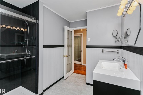 Bathroom featuring a glass-enclosed shower with dark tiling, a modern vanity with a white countertop and basin, and wainscoting along the walls - 24 Sable Crescent, St. Albert, AB - Indoor Photo Showing Bathroom