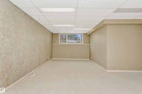 This spacious room features neutral-toned carpet flooring, a drop ceiling with integrated lighting, and a large window providing natural light - 24 Sable Crescent, St. Albert, AB - Indoor Photo Showing Other Room