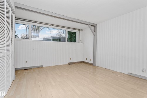 The room features light-toned wood flooring, a window offering views of trees and the sky, and white louvered closet doors - 24 Sable Crescent, St. Albert, AB - Indoor Photo Showing Other Room