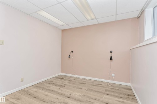 This room features wood-look flooring, a drop ceiling with fluorescent lighting, and two wall-mounted light fixtures - 24 Sable Crescent, St. Albert, AB - Indoor Photo Showing Other Room