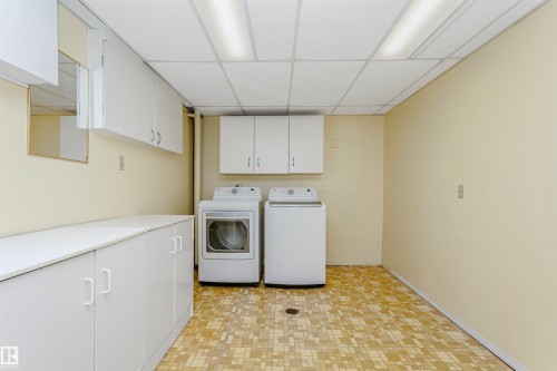 This utility room features extensive white cabinetry, a drop ceiling with fluorescent lighting, and a patterned tile floor - 24 Sable Crescent, St. Albert, AB - Indoor Photo Showing Laundry Room