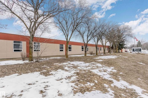 The property features a long, single-story building with multiple windows, set against a backdrop of bare trees and a partially snow-covered ground - 24 Sable Crescent, St. Albert, AB - Outdoor
