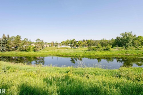 This property offers views of a serene body of water, bordered by lush green grass and mature trees - 24 Sable Crescent, St. Albert, AB - Outdoor With Body Of Water With View