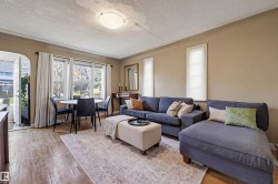 Living area featuring wood-finish flooring, a contemporary ceiling light fixture, and multiple windows with natural light - 