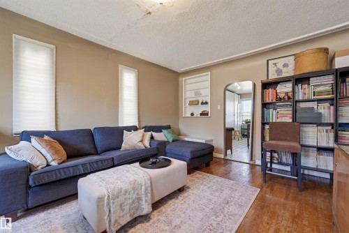 Living space featuring wood-finish flooring, two vertical windows with privacy blinds, and a built-in wall shelf - 9816 93 Avenue, Edmonton, AB - Indoor Photo Showing Living Room