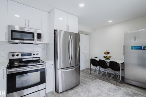 Contemporary kitchen featuring white cabinetry, stainless steel appliances, wood-finish flooring, recessed lighting, and a dining area - 236 Lago Lindo Crescent, Edmonton, AB - Indoor Photo Showing Kitchen With Upgraded Kitchen