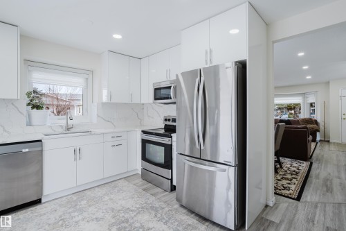 Modern kitchen featuring white glossy cabinetry, stainless steel appliances, marble-patterned countertops, and wood-finish flooring - 236 Lago Lindo Crescent, Edmonton, AB - Indoor Photo Showing Kitchen With Upgraded Kitchen