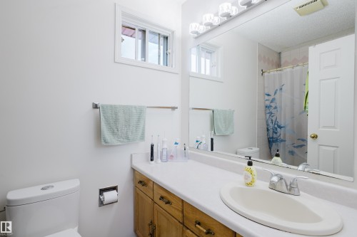 Bathroom featuring a wood-finish vanity with a white countertop and an integrated sink, a large wall-mounted mirror, overhead vanity lighting, and a white toilet - 236 Lago Lindo Crescent, Edmonton, AB - Indoor Photo Showing Bathroom