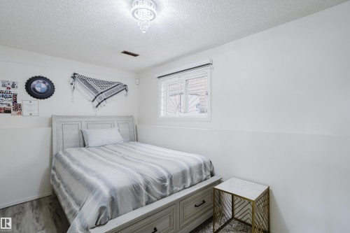 Bedroom featuring a window with white blinds, wood-finish flooring, and a decorative ceiling light fixture - 236 Lago Lindo Crescent, Edmonton, AB - Indoor Photo Showing Bedroom