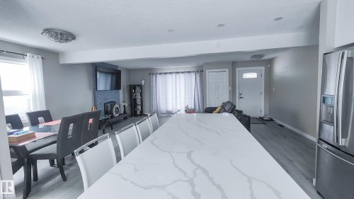 Expansive kitchen island with a quartz countertop, recessed lighting, wood-finish flooring, a contemporary dining fixture, and stainless steel appliances - 3311 108 Street, Edmonton, AB - Indoor