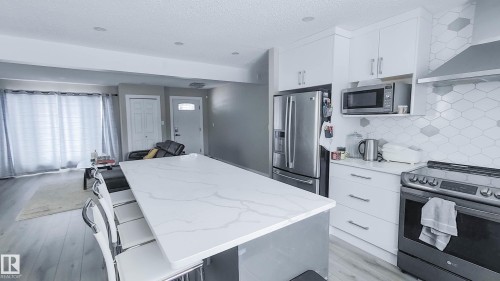 Contemporary kitchen featuring an oversized island with a stone countertop, white shaker-style cabinetry, stainless steel appliances, and geometric tile backsplash - 3311 108 Street, Edmonton, AB - Indoor Photo Showing Kitchen