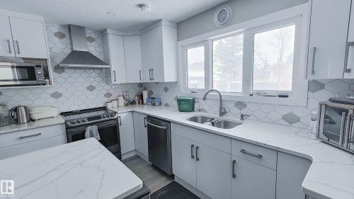Kitchen featuring white cabinetry, light-toned countertops, a stainless steel range hood, a double basin sink with a gooseneck faucet, and a geometric-patterned backsplash - 3311 108 Street, Edmonton, AB - Indoor Photo Showing Kitchen With Double Sink With Upgraded Kitchen