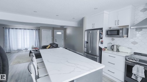 Kitchen featuring a large central island with a patterned countertop, white cabinetry, stainless steel appliances, and a geometric tile backsplash - 3311 108 Street, Edmonton, AB - Indoor Photo Showing Kitchen With Upgraded Kitchen