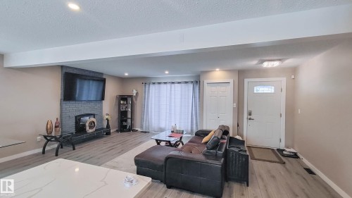 Spacious living area featuring light wood-finish flooring, recessed lighting, and a prominent grey brick-style fireplace with a dark mantel - 3311 108 Street, Edmonton, AB - Indoor Photo Showing Living Room With Fireplace