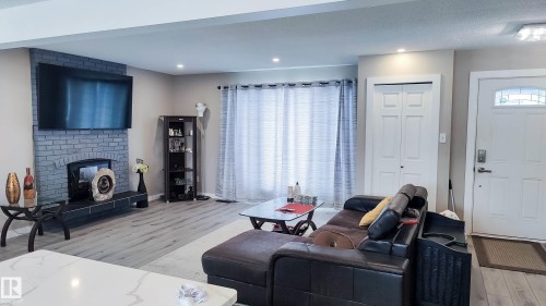 Living room featuring a grey brick fireplace with a hearth, wood-finish flooring, recessed lighting, and a front entry door with an arched glass insert - 3311 108 Street, Edmonton, AB - Indoor Photo Showing Other Room With Fireplace