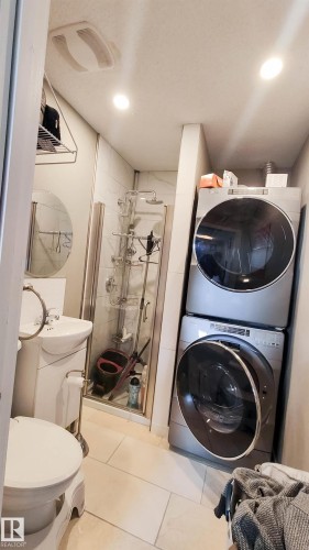 Compact bathroom featuring a shower stall with a glass enclosure, a pedestal sink, and a stacked washer and dryer unit - 3311 108 Street, Edmonton, AB - Indoor Photo Showing Laundry Room