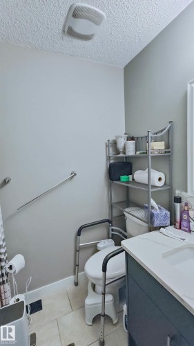 Bathroom featuring light gray walls, tile flooring, a dark gray vanity with a light countertop, a toilet, and a wall-mounted towel bar - 3311 108 Street, Edmonton, AB - Indoor