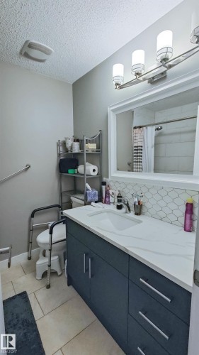 Bathroom featuring a dark blue vanity with a white countertop and integrated sink, a large framed mirror, and a three-light fixture - 3311 108 Street, Edmonton, AB - Indoor Photo Showing Bathroom