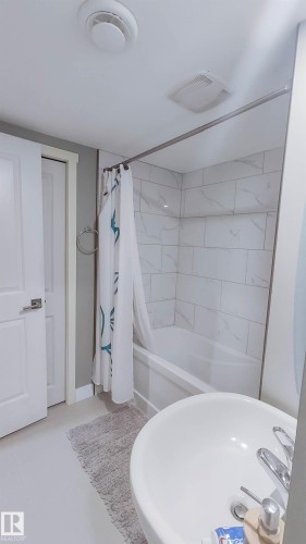 Bathroom featuring a white bathtub, white tile surround, and a round basin sink - 3311 108 Street, Edmonton, AB - Indoor Photo Showing Bathroom