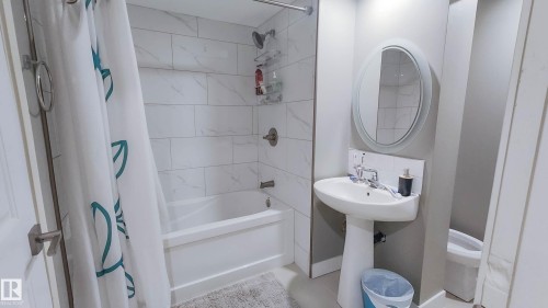 Bathroom featuring a pedestal sink, oval mirror, and a full bathtub with a tile surround and shower fixtures - 3311 108 Street, Edmonton, AB - Indoor Photo Showing Bathroom