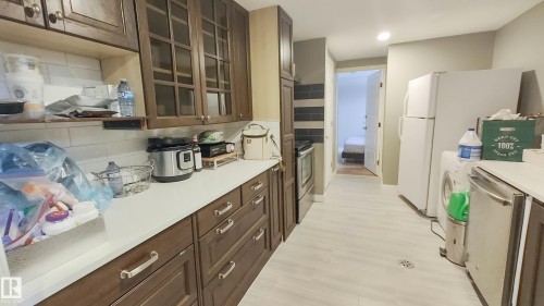 Kitchen featuring dark wood-finish cabinetry with glass door accents, a white subway tile backsplash, light-colored countertops, a stainless steel oven, and light wood-finish flooring - 3311 108 Street, Edmonton, AB - Indoor Photo Showing Kitchen