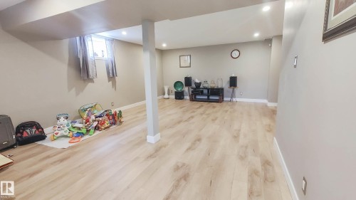 Spacious interior featuring light wood-finish flooring, recessed lighting, neutral wall paint, white trim, and a window with curtain rods - 3311 108 Street, Edmonton, AB - Indoor